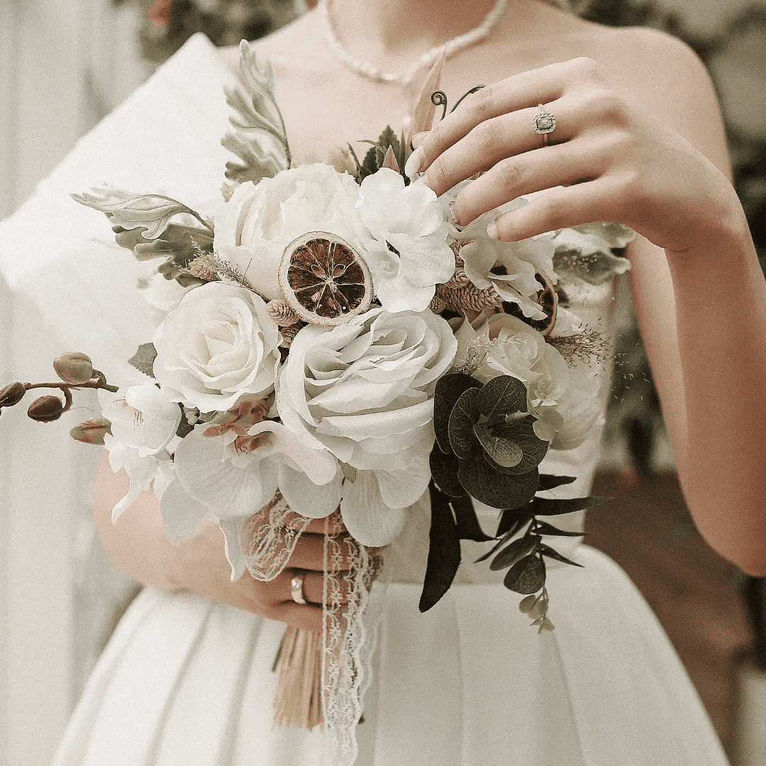 Bride holding a white floral bouquet near a window, showcasing her wedding ring.