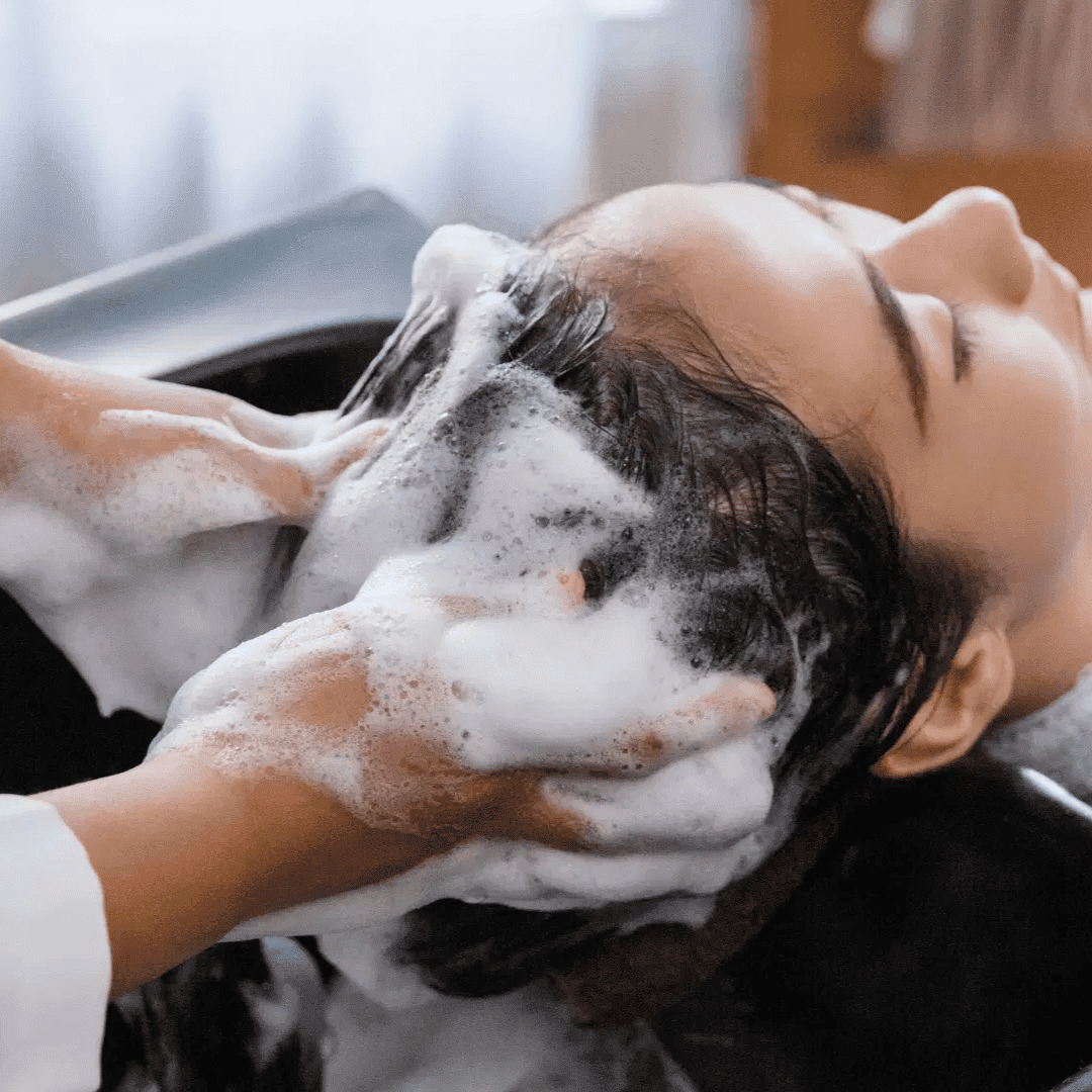 Person receiving a relaxing, professional hair wash with foamy shampoo in a salon.