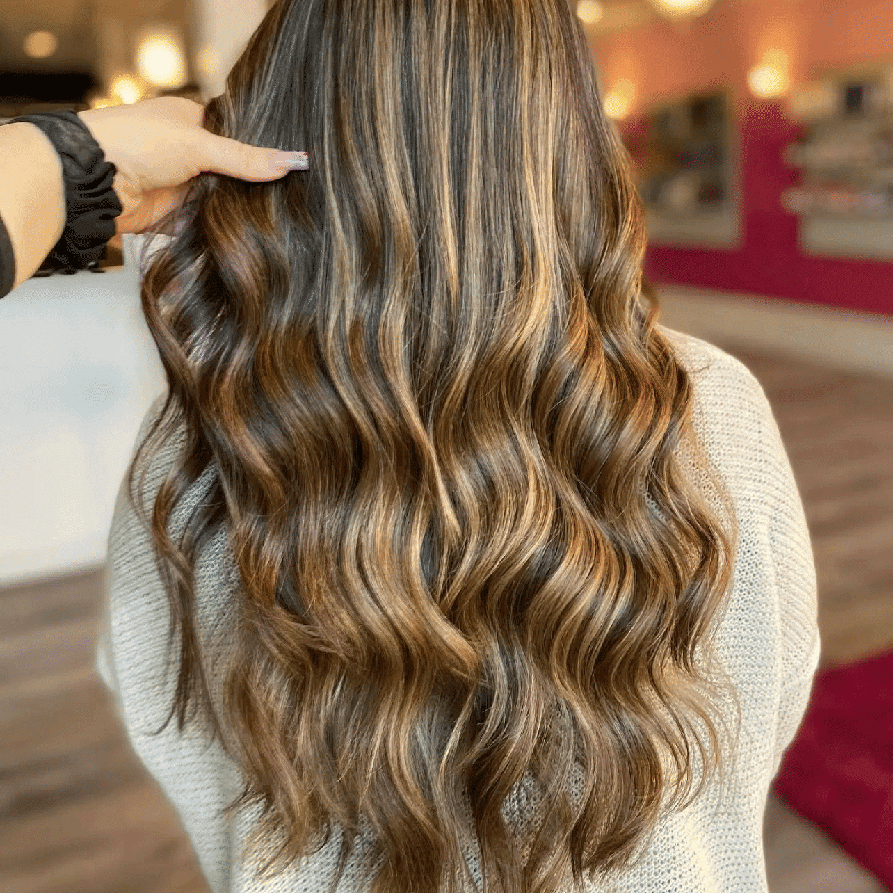 Wavy hair with highlights in a salon setting, styled by a stylist's hand.