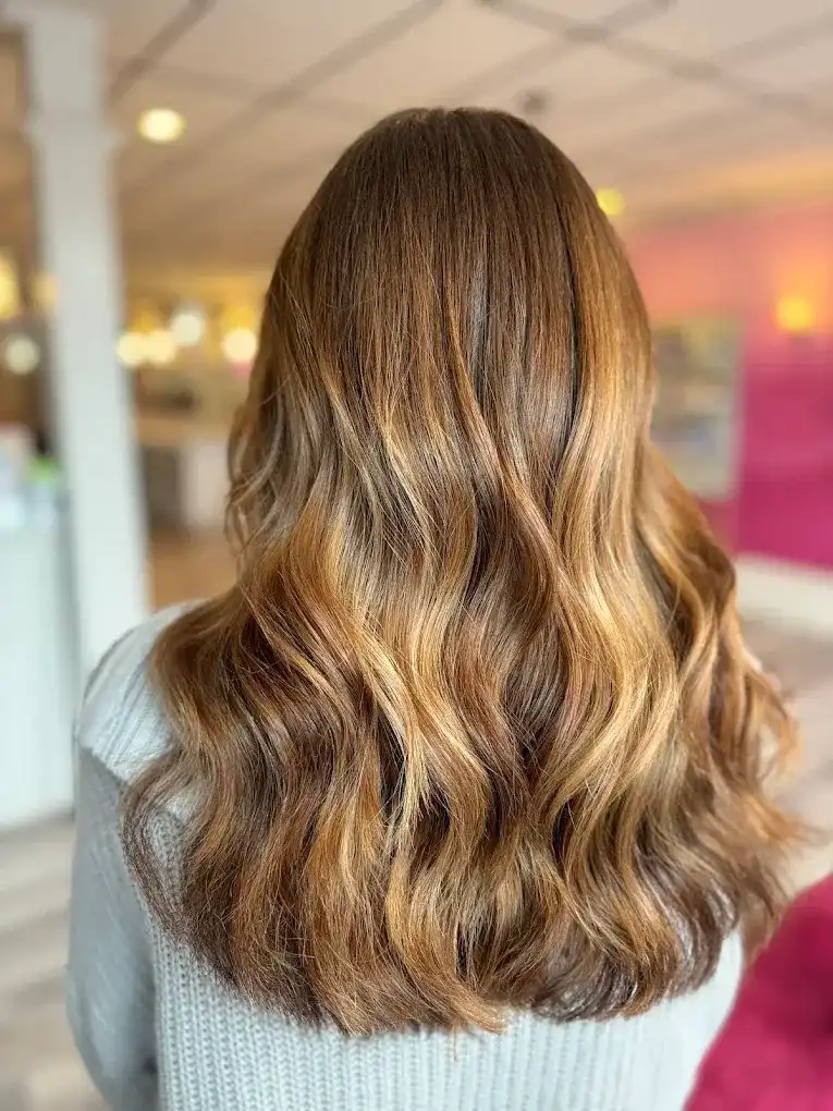 Woman with wavy, light brown hair viewed from the back in a brightly lit salon.