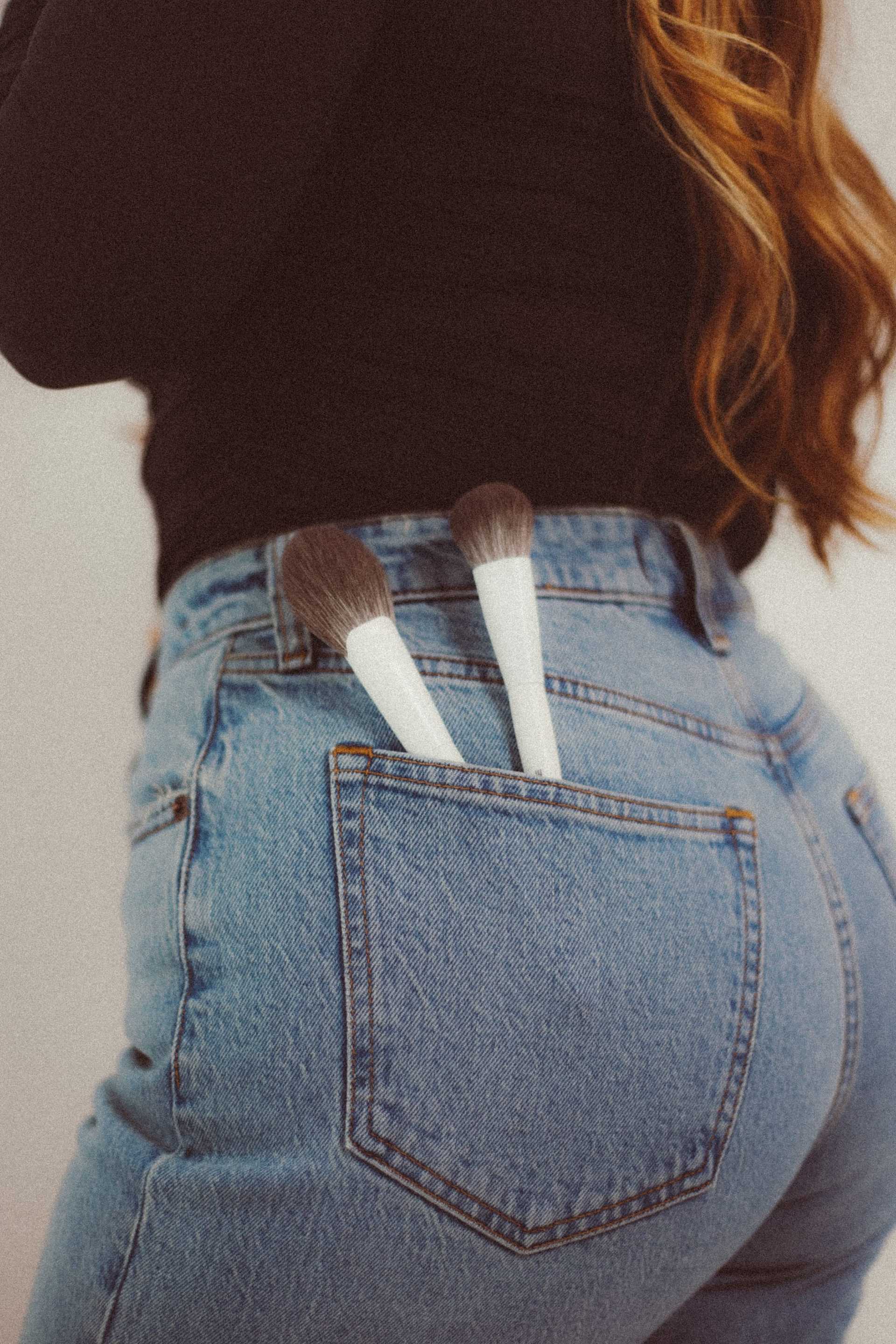 Makeup brushes in a back pocket of blue jeans.